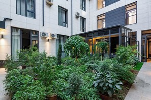 A courtyard with potted plants, a glass door entrance, and a building with multiple windows and air conditioning units. - Beshchinor Hotel (Tashkent)