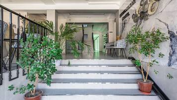 A hotel lobby with a staircase, potted plants, and a marble wall with a sign.