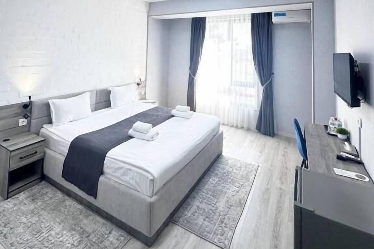 A modern hotel room with a large bed, bedside tables, a desk, and a flat-screen TV.