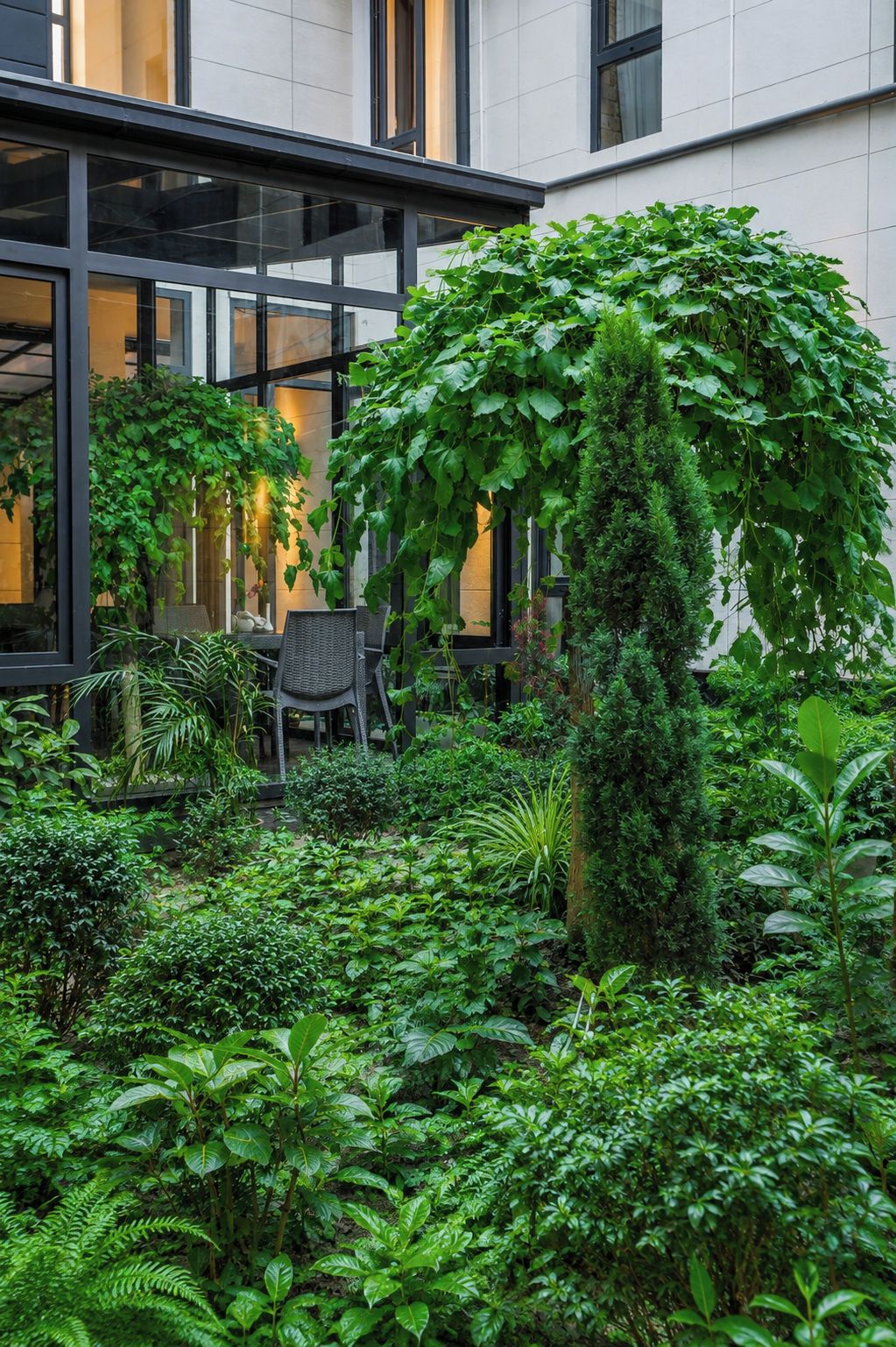 A lush indoor garden with various plants and a seating area.