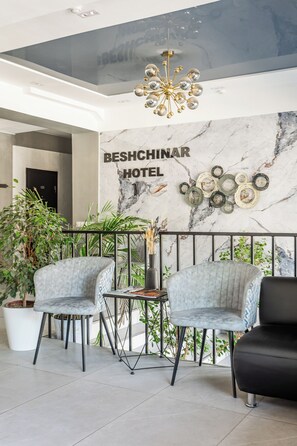 A reception area with a marble wall, a chandelier, and two grey upholstered chairs. - Beshchinor Hotel  (Tashkent)