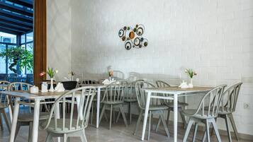 A dining area with white brick walls, grey chairs, and tables. There are decorative wall art pieces and potted plants on the tables.