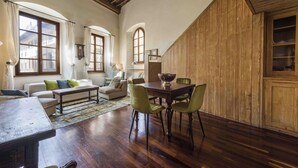 Ein geräumiger Raum mit einem Holztisch, grünen Stühlen, einer Couch mit Kissen und einem großen Fenster.