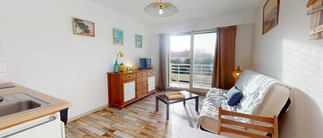 Eine moderne Wohnung mit Küche, Essbereich und Wohnzimmer. Sie verfügt über einen Holzboden, ein Sofa, einen Fernseher und einen Balkon mit Blick.