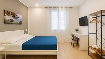 A bedroom with a bed, a desk, a chair, a TV, and a wardrobe.