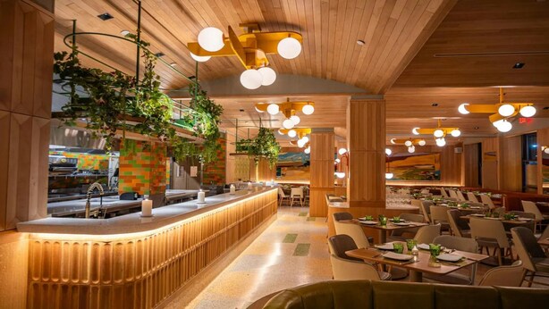 Interior de un restaurante con techo de madera, plantas colgantes e iluminación circular.