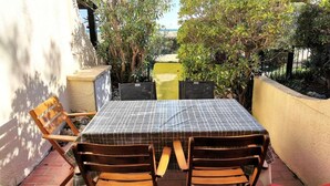 En terrasse med et bord og fire stole, omgivet af planter og en mur.