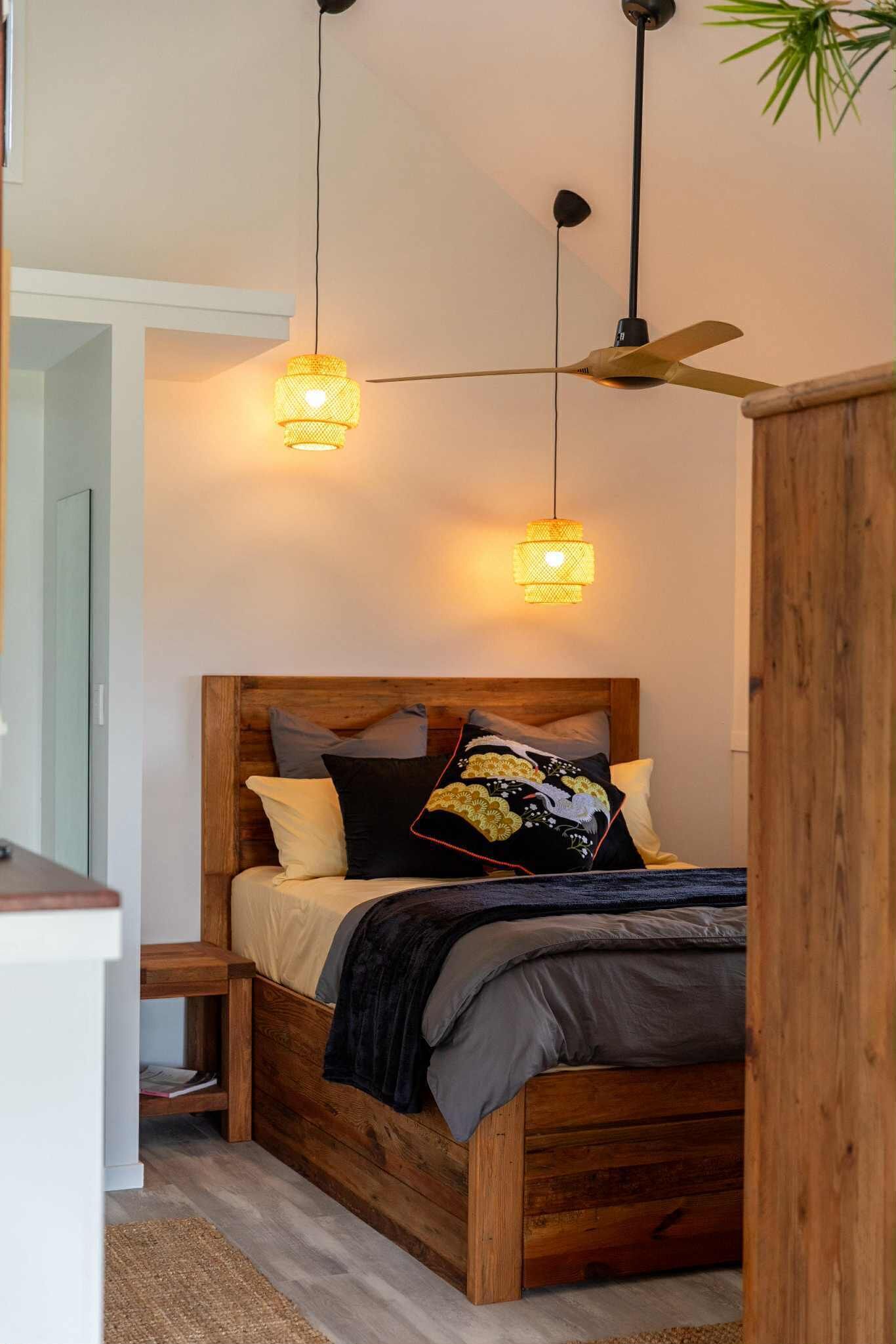 Un dormitorio con una cama de madera, dos lámparas colgantes y un ventilador de techo.