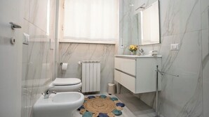 Une salle de bain moderne équipée de toilettes, d’un bidet et d’un lavabo, avec des murs en marbre et un grand miroir.