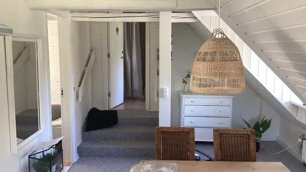Een kamer met een houten tafel, rieten stoelen, een witte dressoir en een hangende rieten lamp.