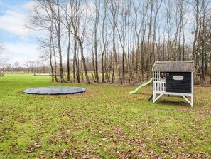 A playground with a slide and a trampoline, surrounded by trees and grass.