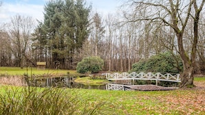 Een park met een vijver, een houten brug en een witte schutting.