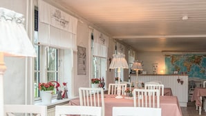 Een gezellig eetgedeelte met witte stoelen en roze tafelkleden, met een wereldkaart aan de muur en een kleine tafel met bloemen en een lamp.