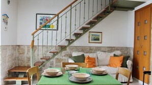 Un comedor con mantel verde, sillas de madera y una escalera con barandillas verdes.