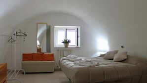 Un dormitorio con cama, ventana, radiador, sofá y espejo.
