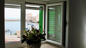 Una habitación con vista al agua y edificios a través de una ventana, con una planta en el alféizar.