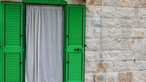 Una pared de piedra con una ventana cubierta por una persiana verde y una puerta, con un letrero pequeño en la pared.