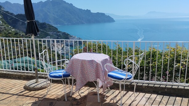Eine Terrasse mit Tisch und Stühlen mit Blick auf die Küste und Berge im Hintergrund.