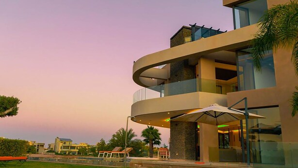 Un edificio moderno a più piani con un balcone curvo, finestre in vetro e posti a sedere all'aperto.