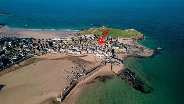 Une vue aérienne d’une ville côtière, avec une plage, une structure fortifiée et une flèche rouge pointant vers un endroit précis.