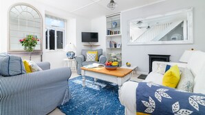 Un salon moderne avec un canapé, une table basse et un téléviseur. On y trouve également une bibliothèque et une cheminée.