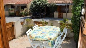 Un patio con un tavolo rotondo e sedie, circondato da un muretto e piante.