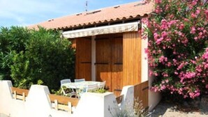 Un piccolo edificio in legno con tetto in tegole, un tavolo con sedie e un vaso con fiori rosa.