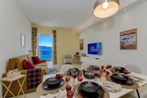 A modern living room with a dining area set for a meal, featuring a sofa, a TV, and a table with plates, glasses, and apples. - Desenzanoloft Garda Golden Sunrise (Desenzano del Garda)