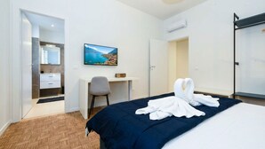Quarto de hotel com cama, escrivaninha, cadeira, televisão e guarda-roupa.