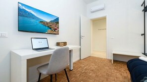 A modern room with a wooden herringbone floor, a white desk with a laptop, a grey chair, a large window with a scenic view, and a door leading to a bathroom. - Desenzanoloft Garda Golden Sunrise (Desenzano del Garda)