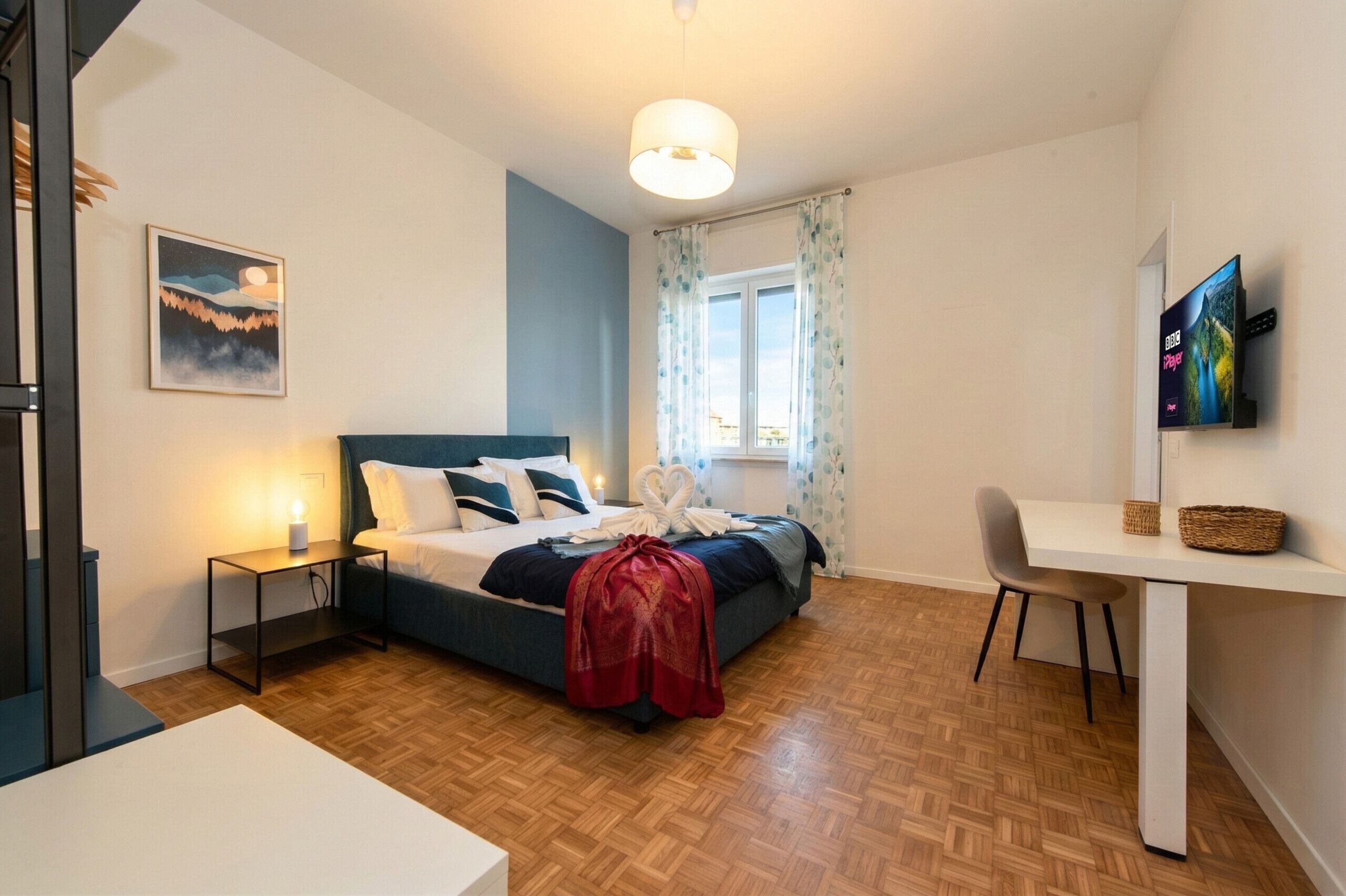 A bedroom with a bed, bedside table, lamp, and a painting on the wall.