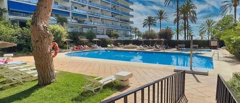 Et poolområde ved hotellet med et klart, blåt pool, liggestole og palmer.