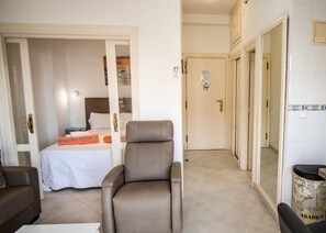 A hotel room with a bed, a brown armchair, a sofa, and a trash bin. - Skol 205 A - Studio 1 Bedroom Apartment Skol building, west Sea Views (Marbella)