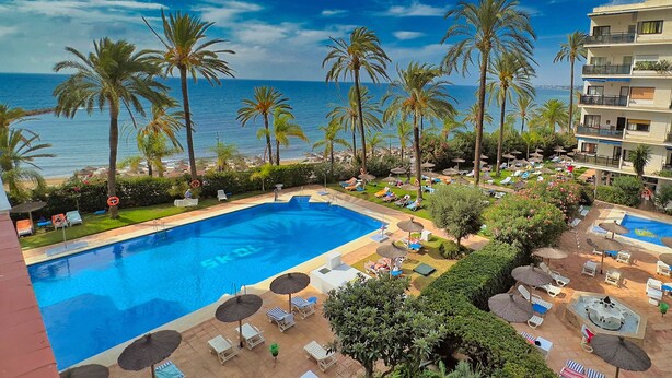 Un complexe hôtelier doté d’une piscine, de chaises longues et de palmiers.