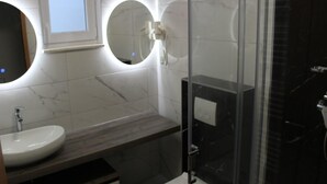 A modern bathroom with a marble vanity, a round mirror, and a glass shower enclosure. - Comfortable Croatian Couple Retreat (Novalja)