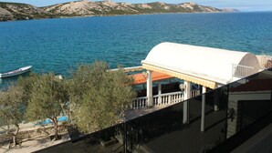 A coastal view with a boat on the water, a white building with a red roof, and a stone wall. - Comfortable Croatian Couple Retreat (Novalja)
