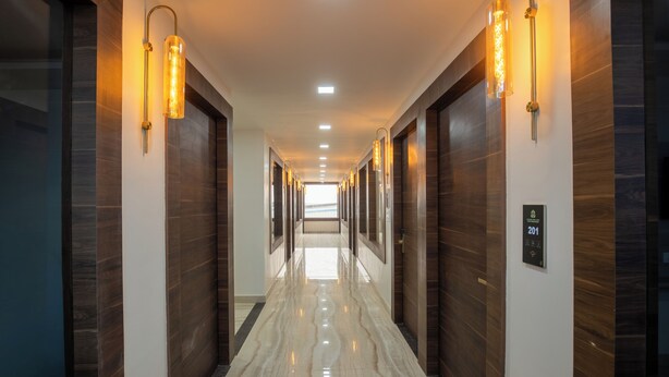 Un couloir d’hôtel moderne avec des murs lambrissés en bois, un sol en marbre et des luminaires fixés au mur.
