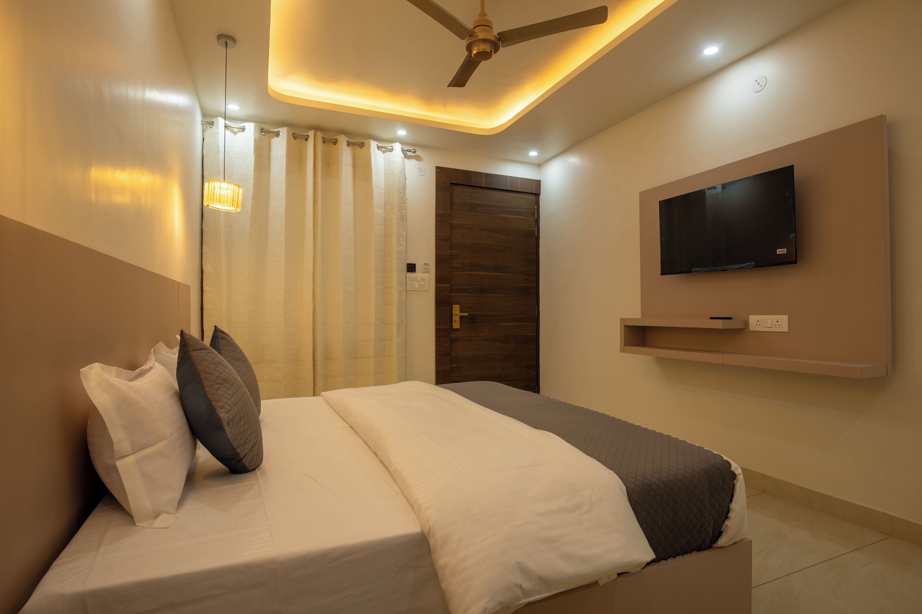 Ein modernes Schlafzimmer mit einem Bett, einem Deckenventilator, einem an der Wand befestigten Fernseher und einer Duschvorhang.