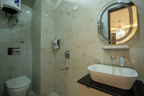 Une salle de bain avec des toilettes blanches, un lavabo doté d’un plan-vasque noir, un miroir avec un cadre doré et un espace douche.