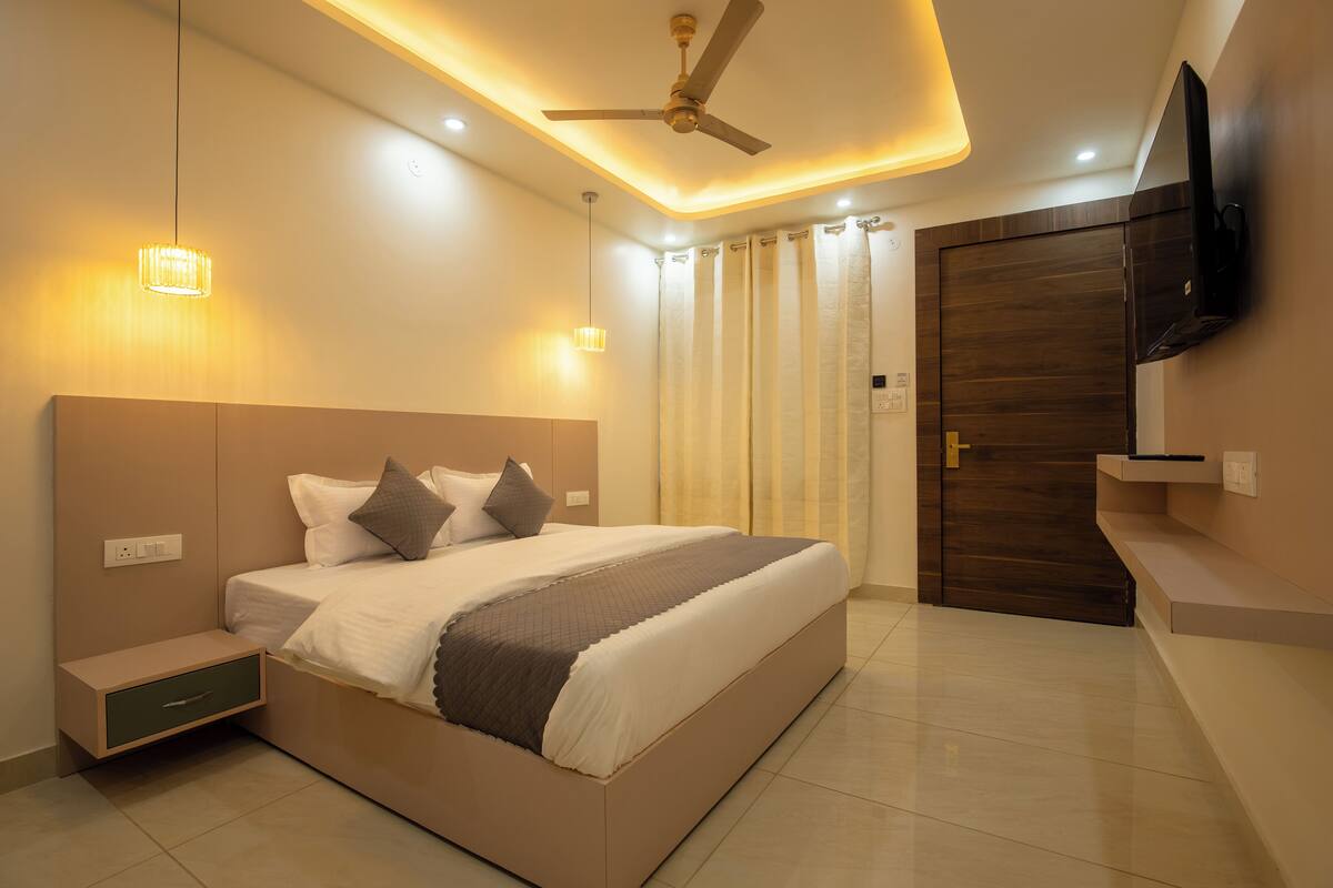 Un dormitorio moderno con una cama grande, un ventilador de techo, luces empotradas, un televisor en la pared y una puerta de madera.