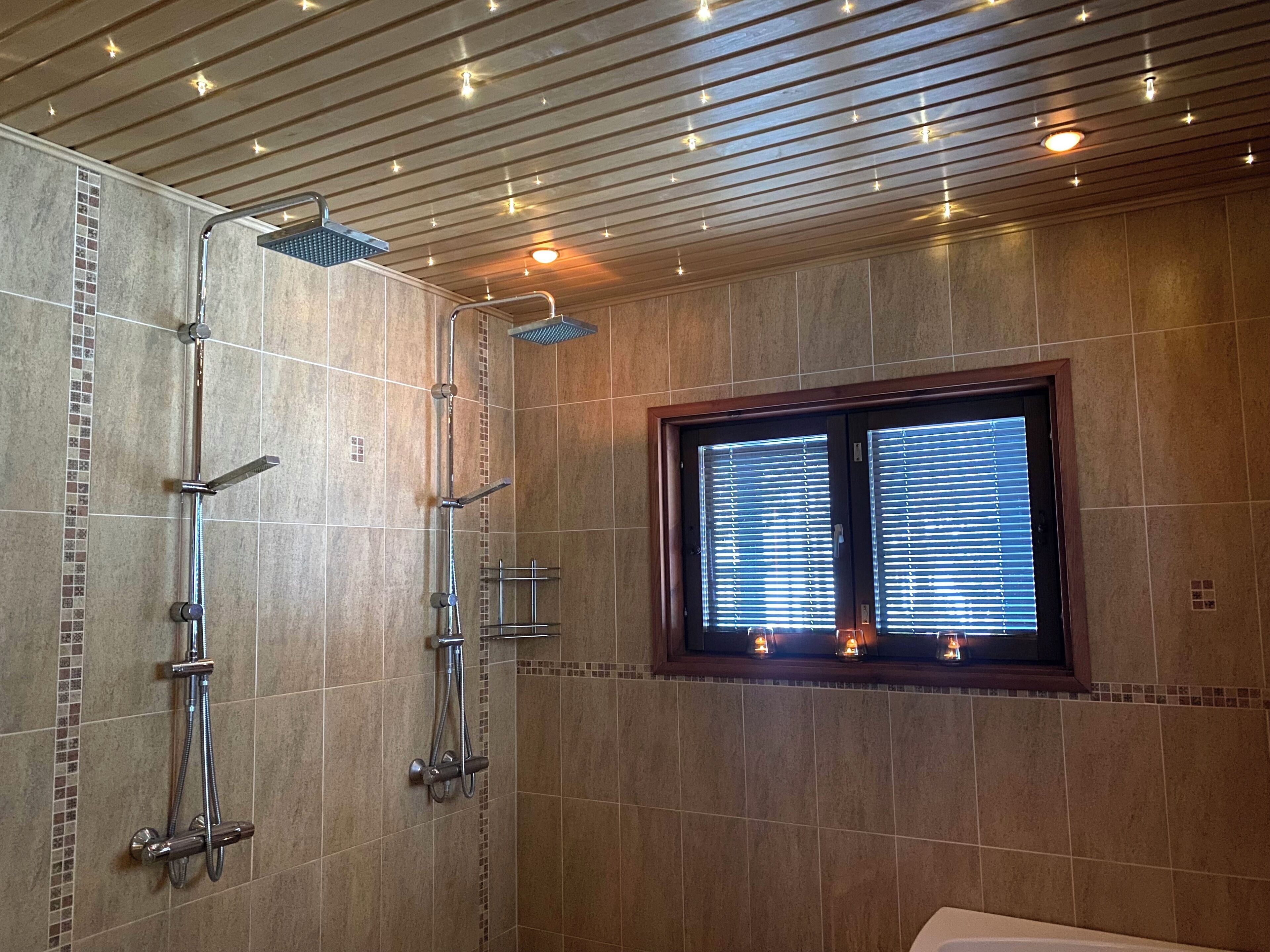 Un baño moderno con ducha a ras de suelo, una ventana con persianas y un techo con iluminación empotrada.