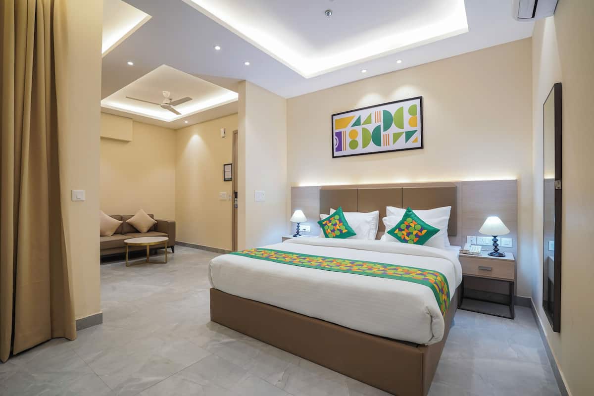 A hotel room with a bed, bedside tables, a sofa, a ceiling fan, and a wall-mounted artwork.