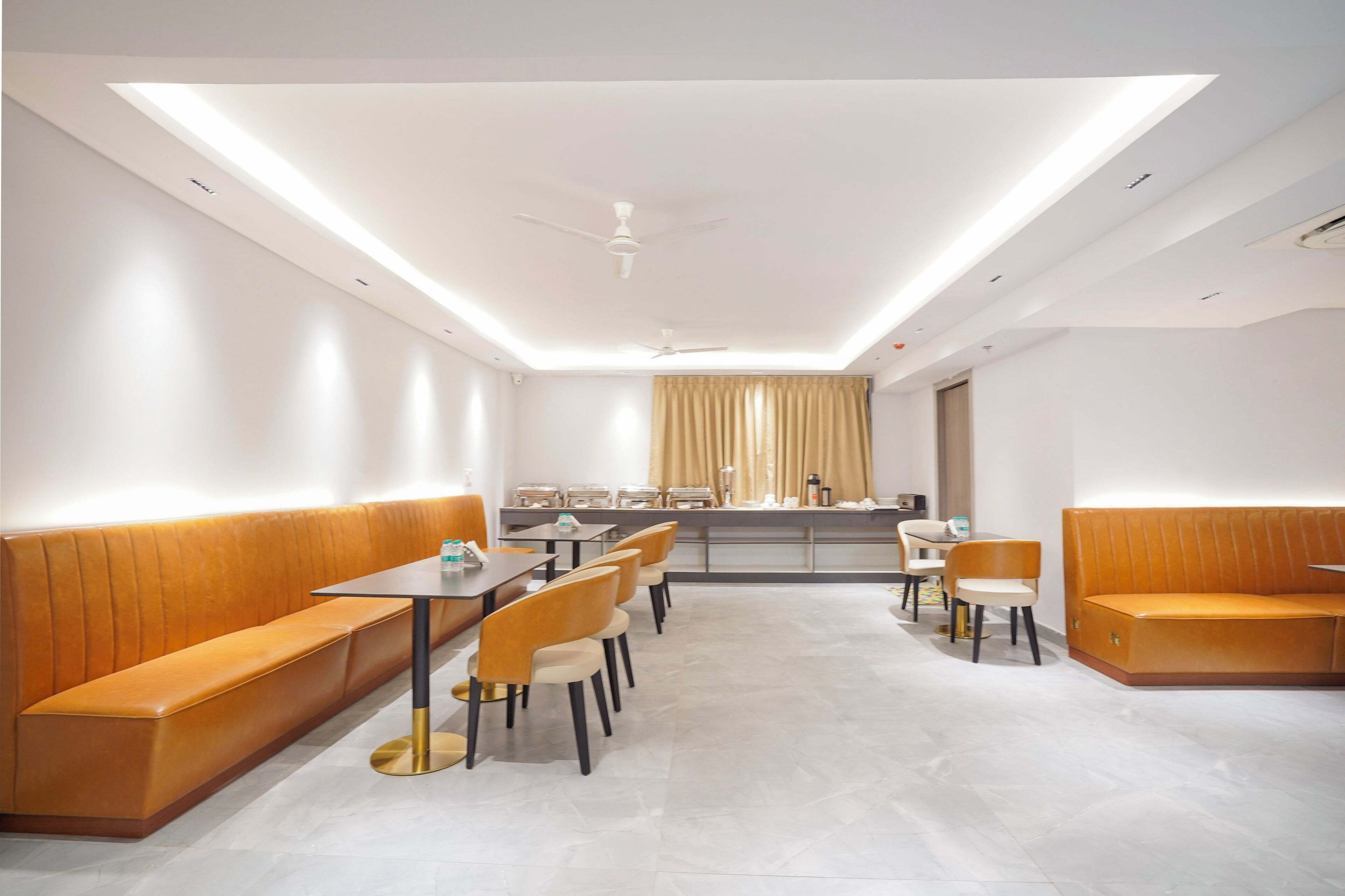 A modern dining area with a long bench, tables, chairs, and a ceiling fan.