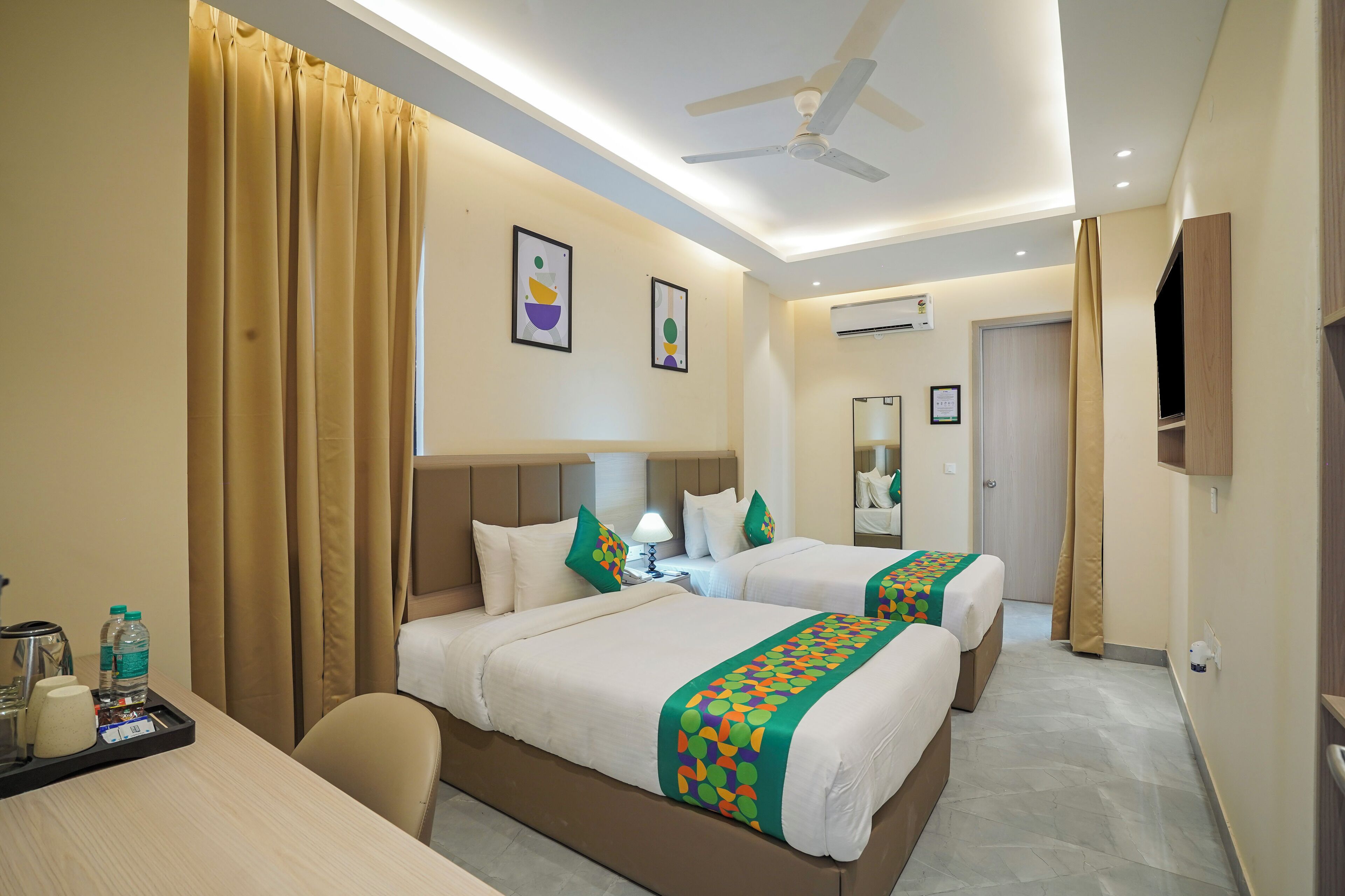 A hotel room with two beds, a desk, a chair, a ceiling fan, and a TV.