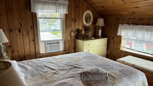 Quarto com cama, cômoda, espelho e janela com vista para casas.