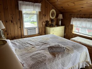 Ein Zimmer mit einem Bett, einem Schminktisch, einem Spiegel und einem Fenster mit Blick auf Häuser.