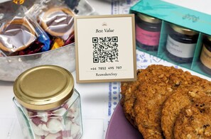 Un código QR, un frasco con tapa, una caja de galletas y frascos de mermelada sobre una mesa.