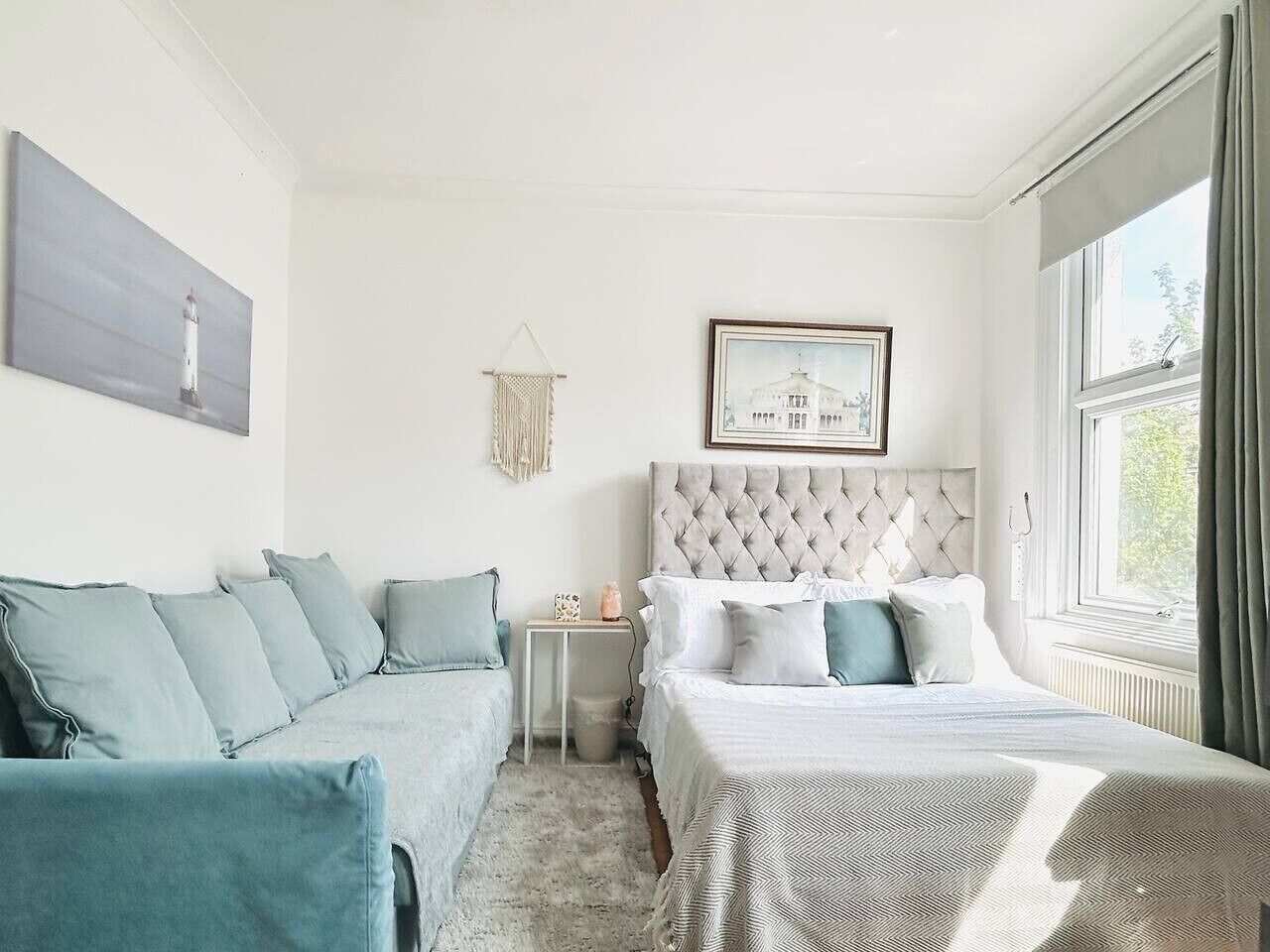 A bedroom with a bed, a sofa, a small table, and a picture on the wall.