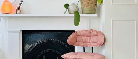 Una sala de estar moderna con chimenea, televisor montado y un sillón rosa.