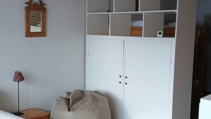 Ett rum med en vit garderob, en sittpuff, ett litet träbord och ett runt bord med ett dukat bord med prickigt mönster.